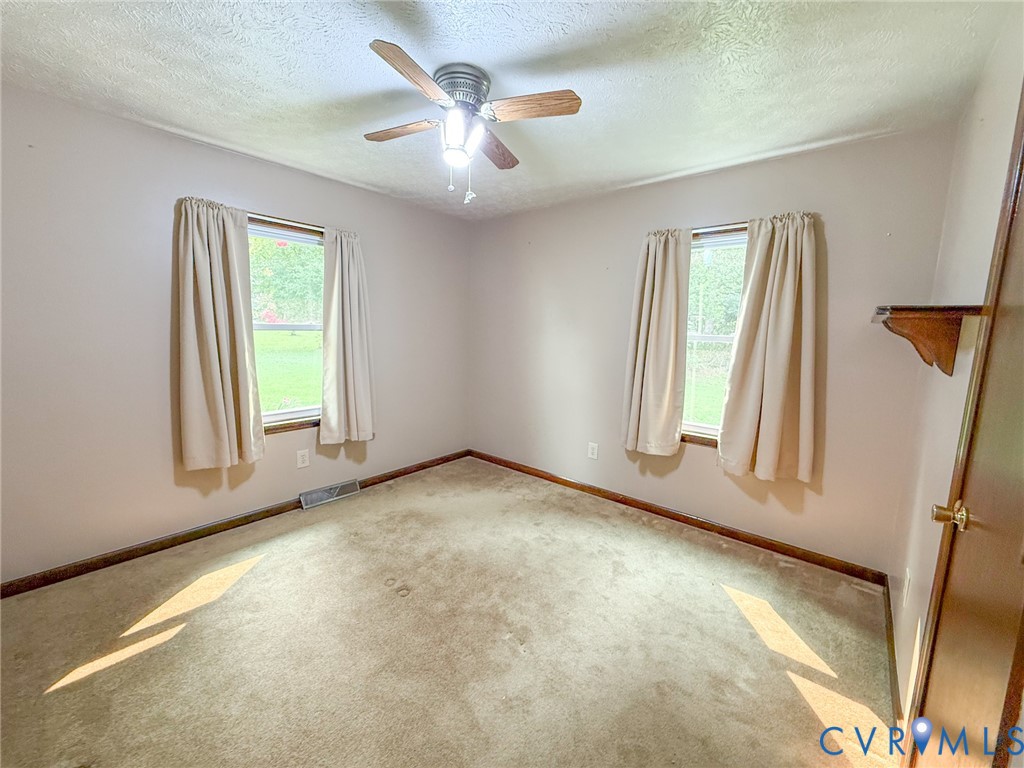 Room with two windows, a ceiling fan with light fixture, and light-colored carpeting