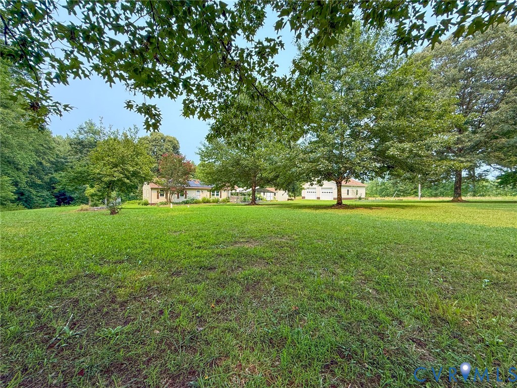 Expansive green lawn with mature trees and a light-colored single-story residence in the background