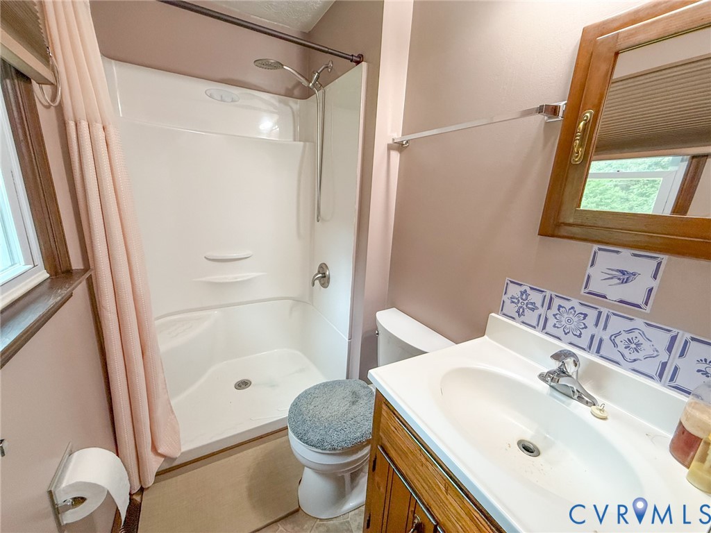 Bathroom featuring a white integrated shower/tub unit, a vanity with a white countertop and basin sink, a wall-mounted mirror with a wood frame, and decorative blue and white tile accents