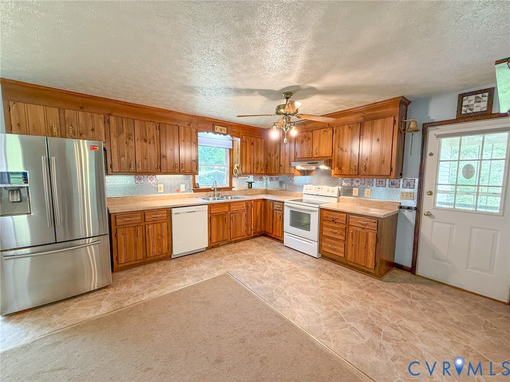 Kitchen featuring extensive wood cabinetry, L-shaped countertops, stainless steel refrigerator, white dishwasher, and white electric range with a matching range hood