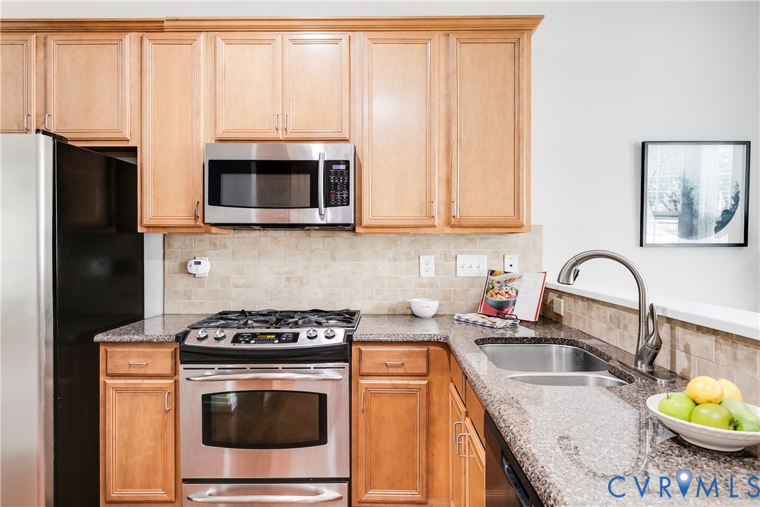 Kitchen featuring wood cabinetry, stainless steel appliances, granite countertops, tile backsplash, and a double basin sink with a gooseneck faucet