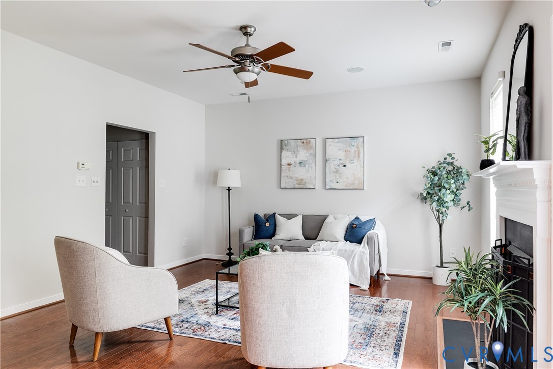 Bright living area featuring wood-finish flooring, a ceiling fan, and a white mantel with a fireplace insert