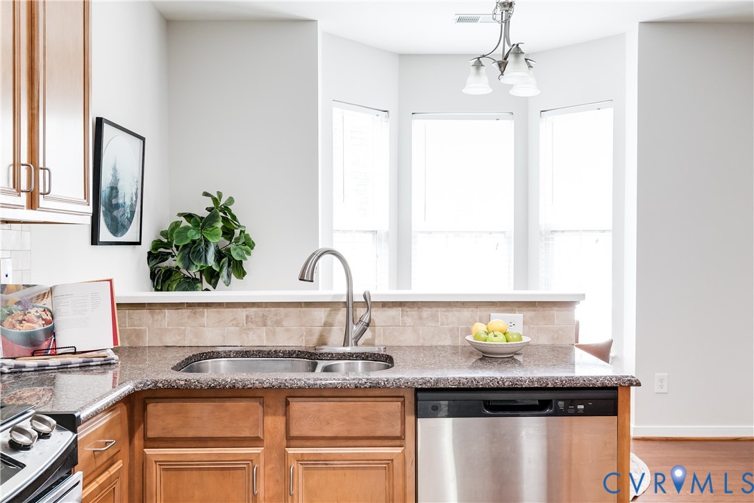 Kitchen featuring wood cabinetry, a double basin stainless steel sink with a gooseneck faucet, a stainless steel dishwasher, and a bay window