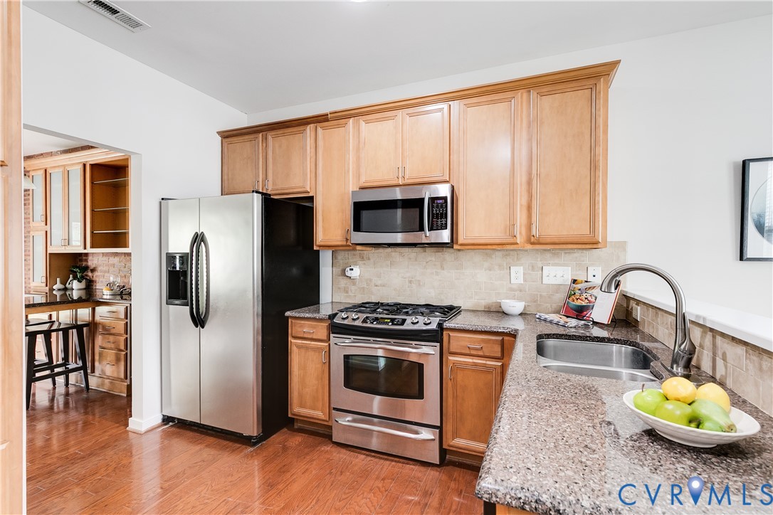Kitchen featuring wood-finish flooring, light wood cabinetry, stainless steel appliances, speckled countertops, and a tile backsplash