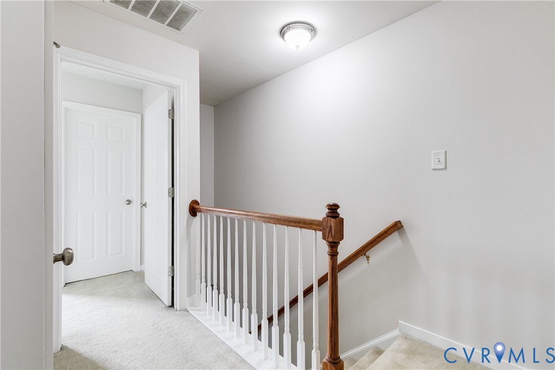 Carpeted hallway featuring a wooden banister with white balusters, leading to a paneled door