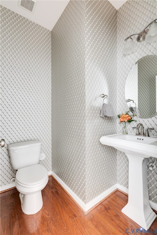 Pedestal sink with chrome faucet, circular mirror, and wall-mounted light fixture