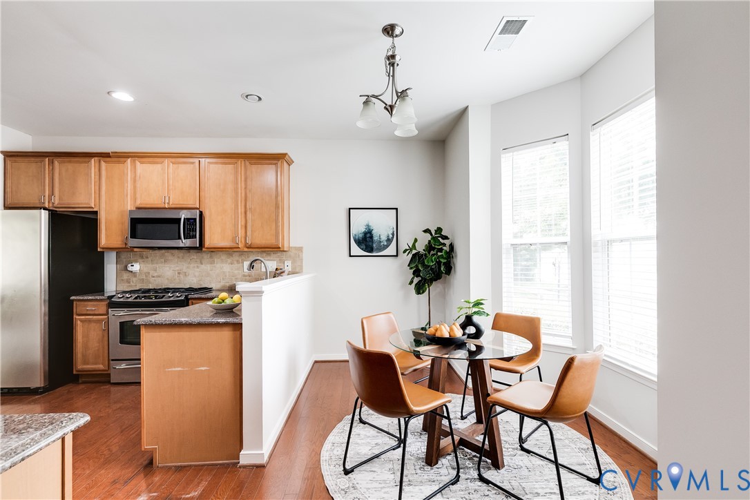 Kitchen and dining area featuring wood-finish flooring, light wood cabinetry, stainless steel appliances, and a tiled backsplash