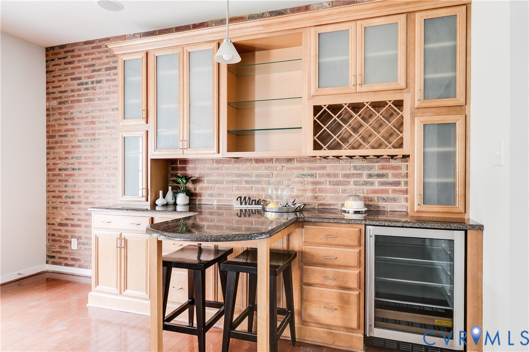 Built-in wet bar featuring light wood cabinetry, brick-patterned wall, integrated wine rack, recessed shelving, and a beverage cooler