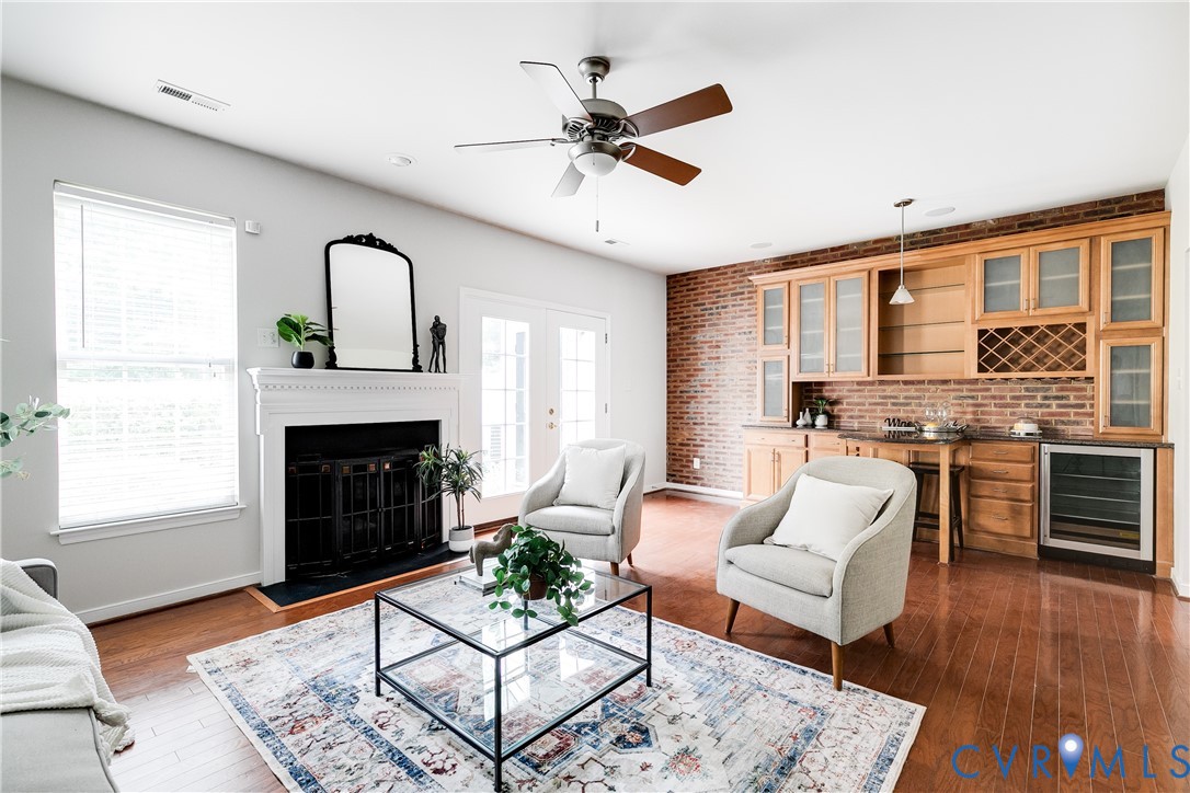 Living space featuring wood-finish flooring, a white-mantled fireplace, and a ceiling fan Living space featuring wood-finish flooring, a white-mantled fireplace, and a ceiling fan