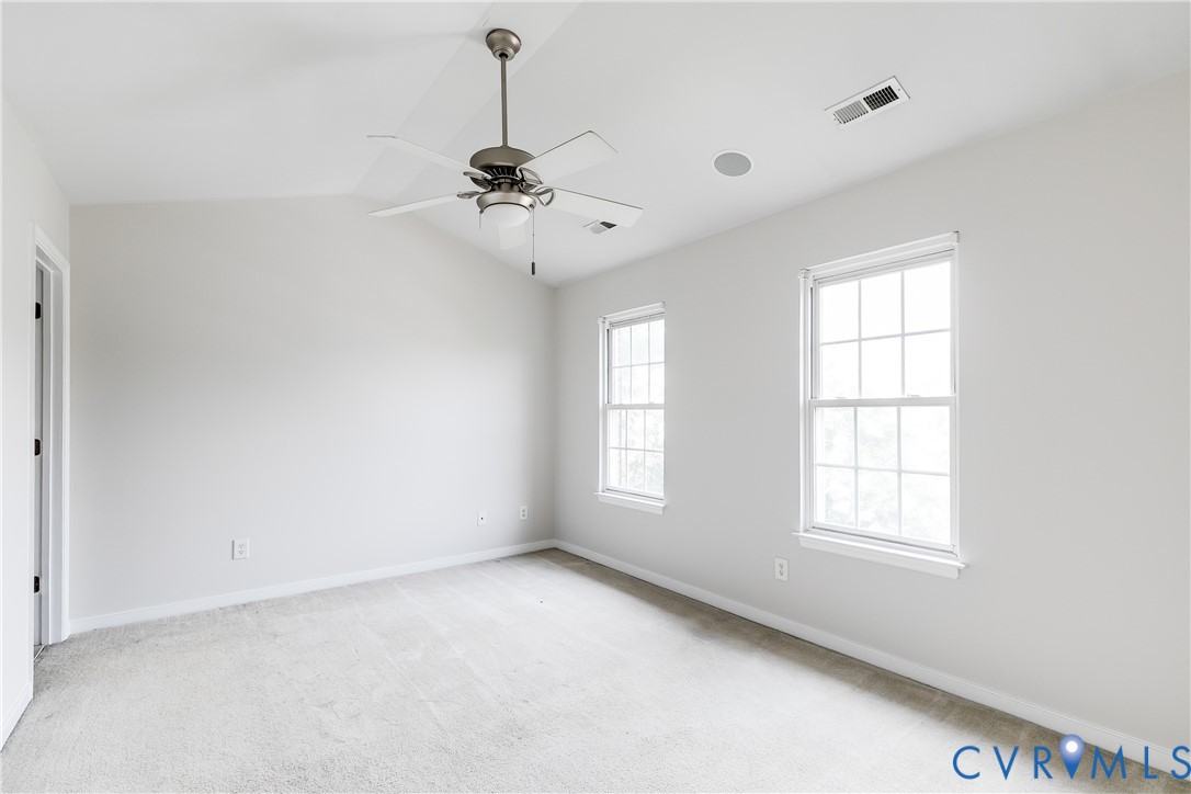 Carpeted room featuring a ceiling fan with integrated lighting, two double-hung windows, a ceiling-mounted speaker, and white baseboards