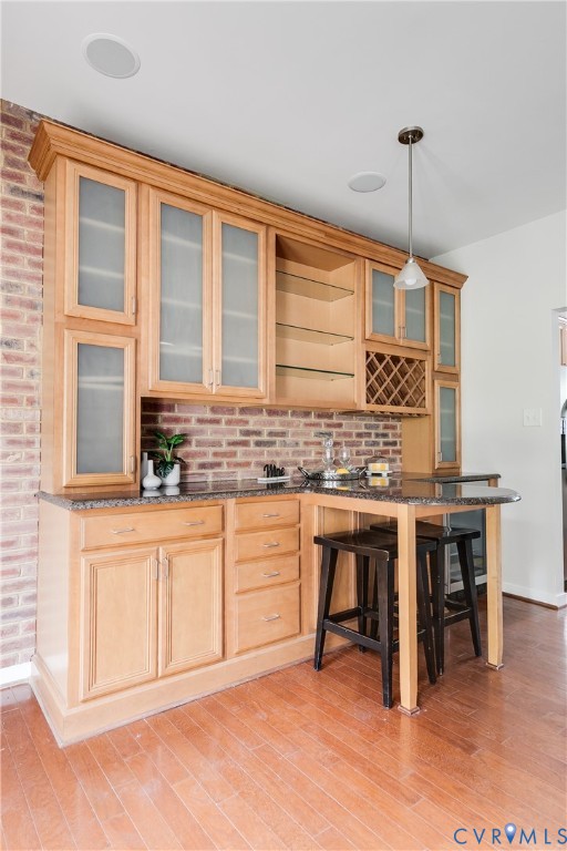 Built-in wet bar featuring wood-finish cabinetry, frosted glass cabinet doors, stone-finish countertops, and an integrated wine rack