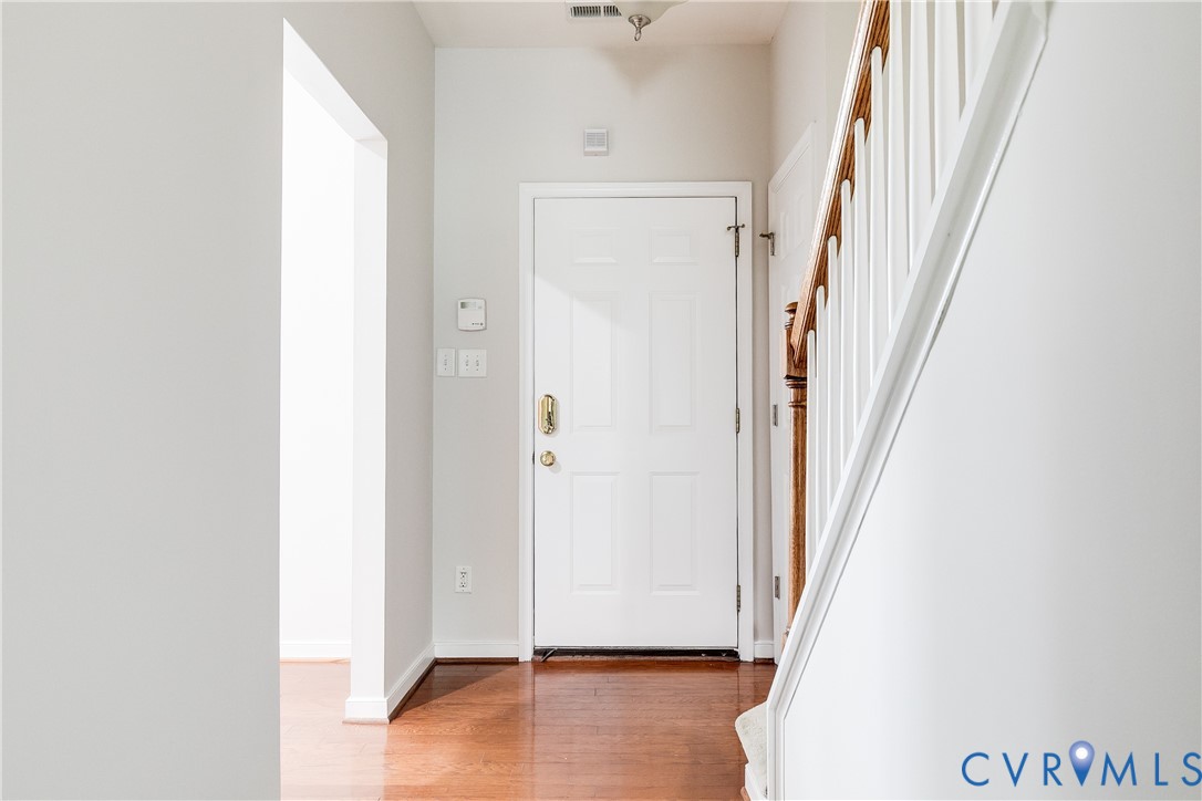 Entryway featuring a paneled door, wood-finish flooring, and a staircase with white risers and a wood handrail