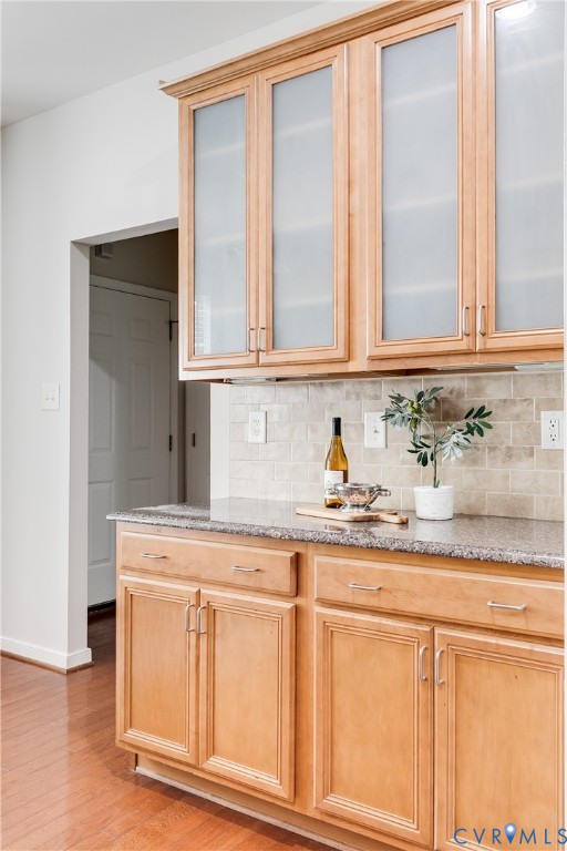 Kitchen featuring light wood-finish cabinetry with frosted glass upper doors, granite-style countertops, and a neutral-toned tile backsplash