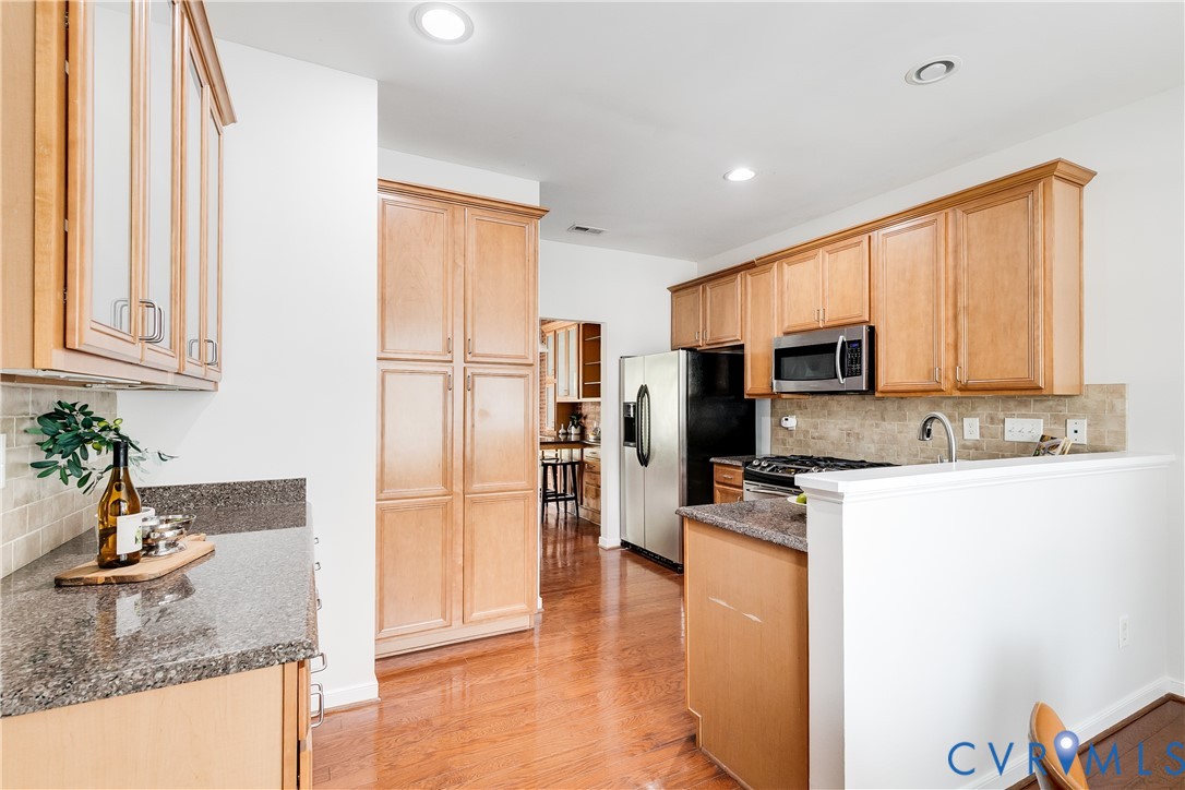 Kitchen featuring wood-finish flooring, recessed lighting, wood cabinetry, stone countertops, and stainless steel appliances