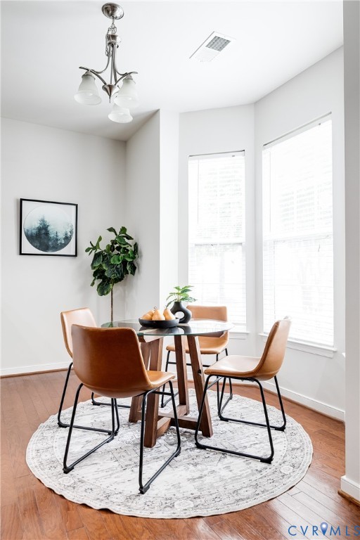 Dining area with wood-finish flooring, a contemporary chandelier, and a bay window featuring multiple large windows