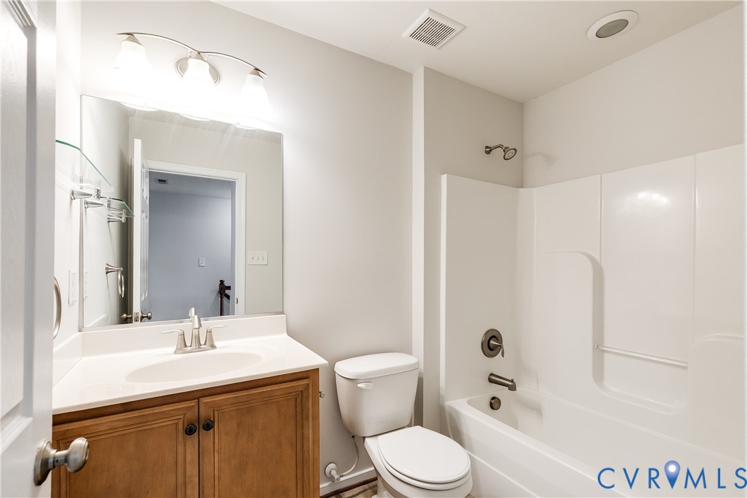 Bathroom featuring a white bathtub/shower combination, a vanity with wood-finish cabinetry, a white countertop, and an integrated sink