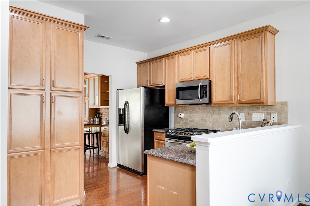 Kitchen featuring wood-finish cabinetry, stainless steel appliances, granite-style countertops, and a tiled backsplash