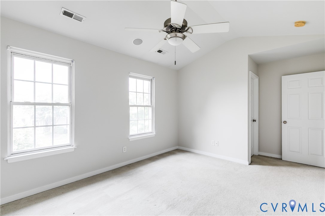 Light-filled room featuring two double-hung windows, a vaulted ceiling, and a ceiling fan with integrated lighting