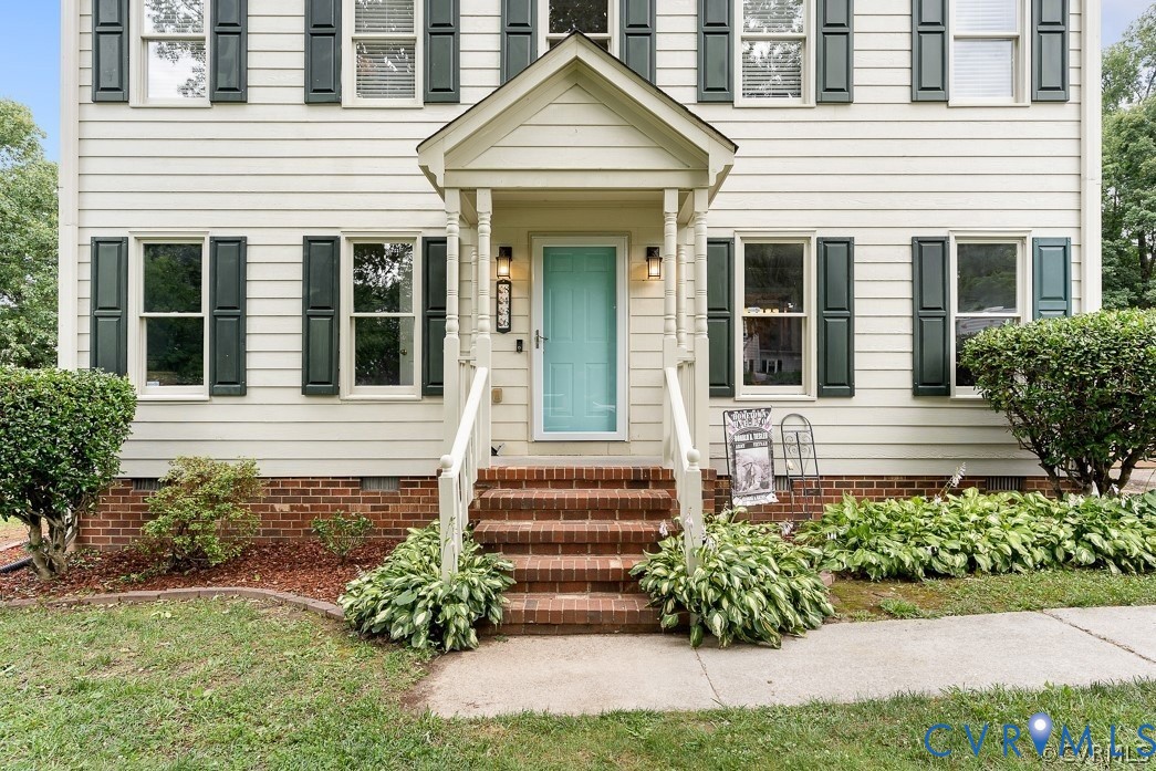 Two-story residence featuring light-toned siding, dark shutters, and a brick foundation