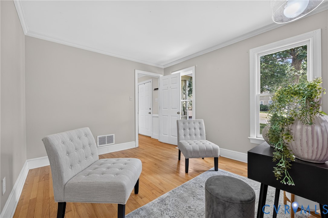 Hardwood flooring, light gray wall paint, crown molding, white trim, and a window providing natural illumination