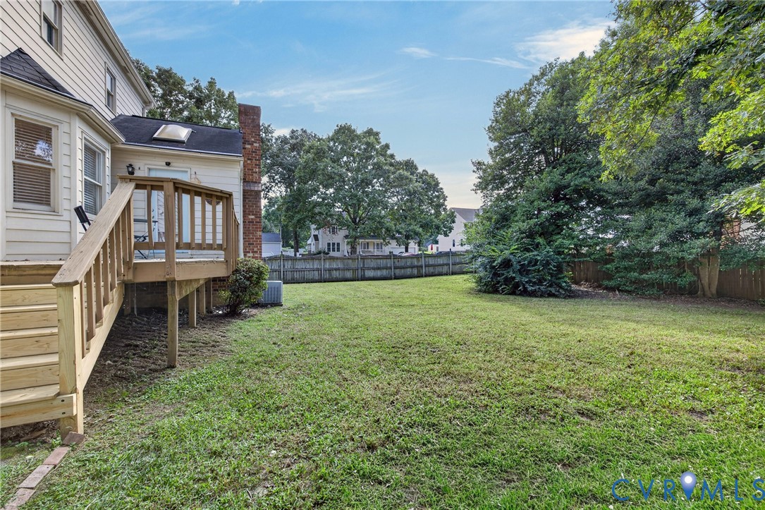 Expansive backyard with a wooden fence, mature trees, and a multi-level wooden deck with stairs