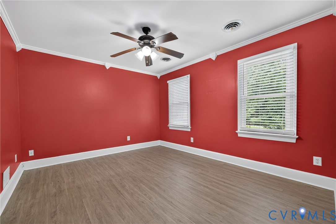 Wood-finish flooring with white trim, two windows with blinds, a ceiling fan, and crown molding