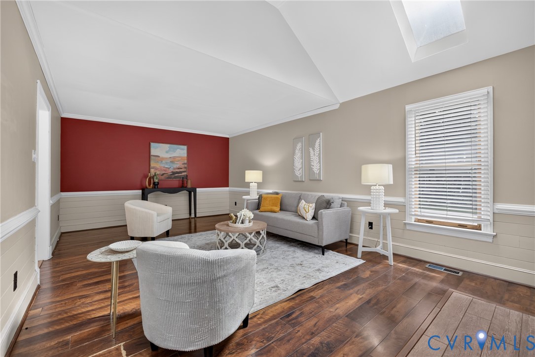Sophisticated living room featuring soaring vaulted ceilings with skylights, rich hardwood flooring throughout, and a striking red accent wall with wainscoting detail