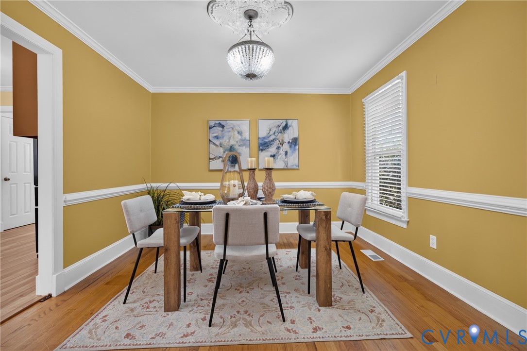 Hardwood flooring, crown molding, chair rail, and a decorative ceiling medallion with a chandelier