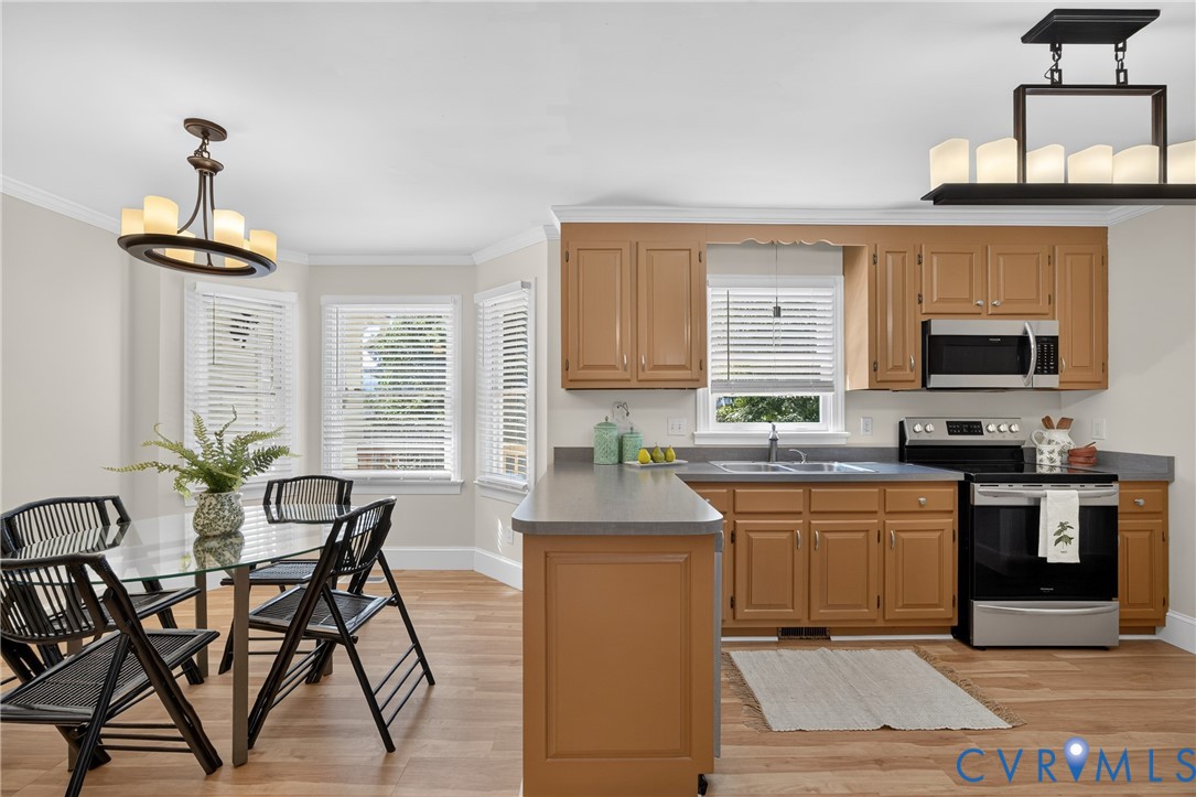 Open-concept kitchen and dining area featuring warm wood-finish cabinetry, stainless steel appliances, gray quartz countertops, and hardwood flooring throughout