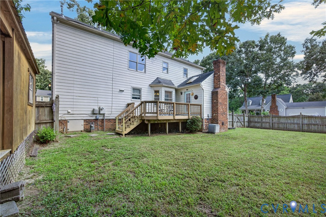 Spacious backyard with mature landscaping and level lawn, accessed via wooden deck with railings