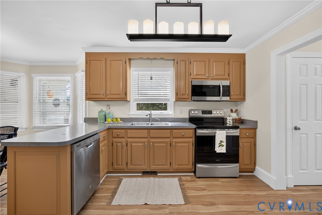 Wood-finish flooring, stainless steel appliances, upper and lower cabinetry, an eat-at counter, and a contemporary chandelier