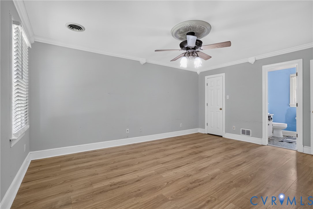 Wood-finish flooring, crown molding, ceiling fan with light fixture, window with blinds, and white interior doors