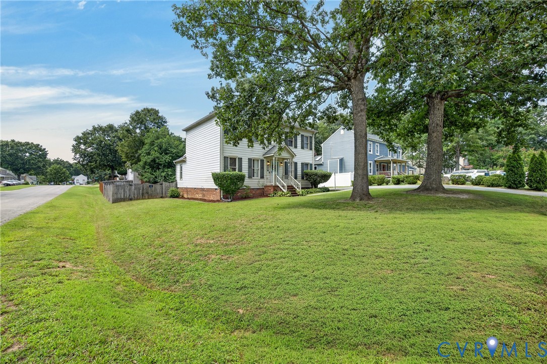 Two-story home with white siding and dark shutters, featuring a front porch with white railings, a brick foundation, and mature trees in the front yard