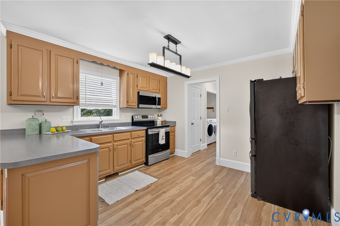 Spacious kitchen featuring wood cabinetry, stainless steel appliances including a gas range and microwave, gray countertops, wood-finish flooring throughout, and abundant natural light from a window over the sink
