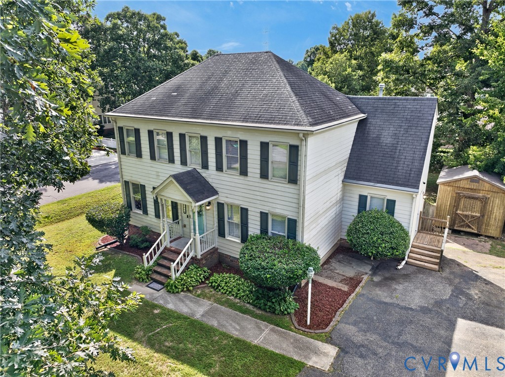 Two-story residence with white siding, dark shutters, covered front porch, paved driveway, and detached storage shed
