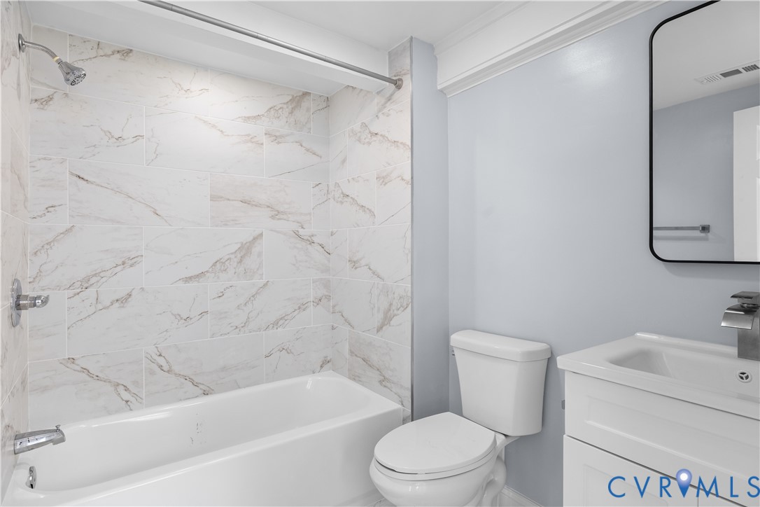Bathtub with white subway tile surround, chrome shower fixtures, white vanity with integrated sink, and contemporary rectangular mirror