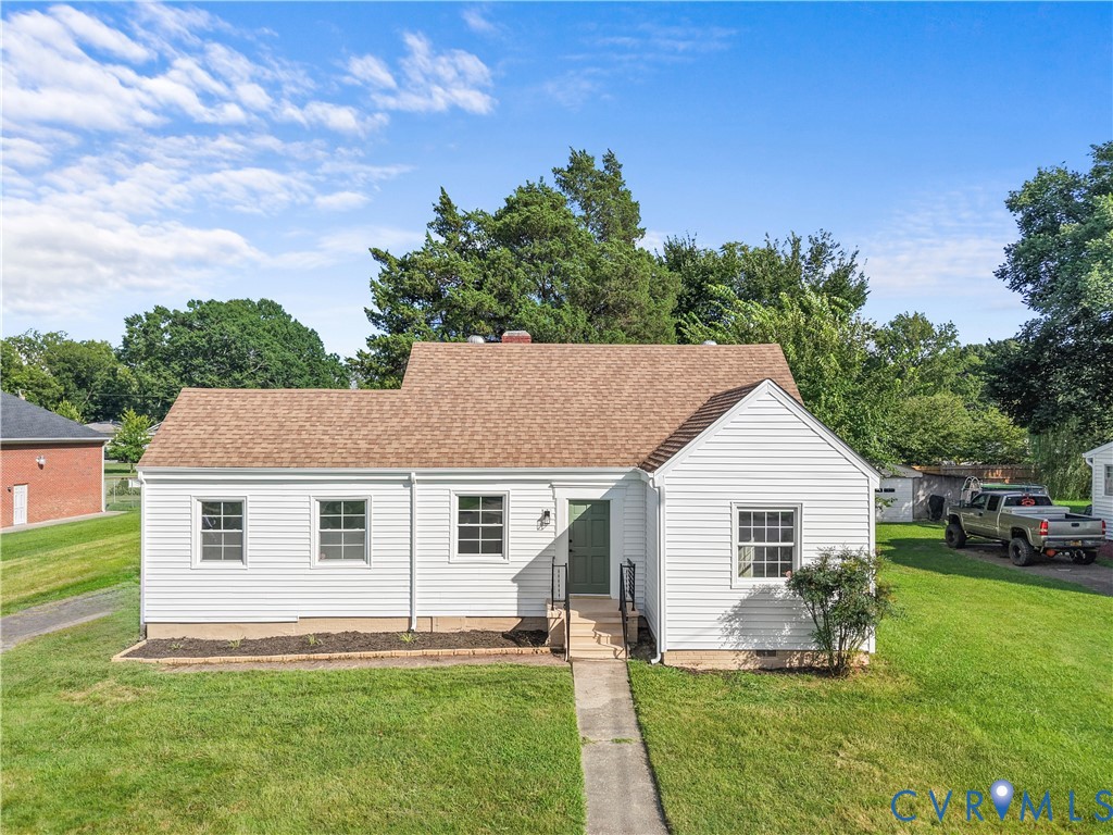 White siding exterior with a brown shingle roof, a green front door, and a concrete walkway White siding exterior with a brown shingle roof, a green front door, and a concrete walkway