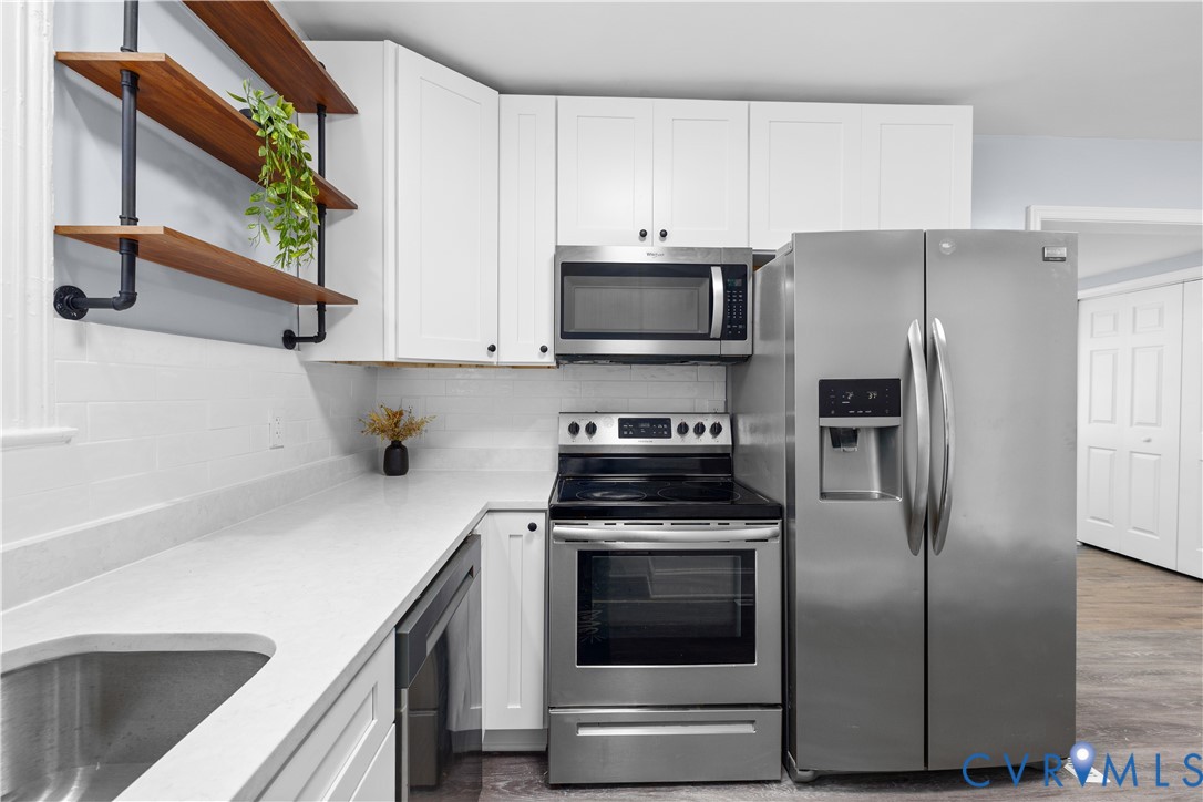 White cabinetry, stainless steel appliances, open wood shelving, light-toned countertops, and a subway tile backsplash White cabinetry, stainless steel appliances, open wood shelving, light-toned countertops, and a subway tile backsplash