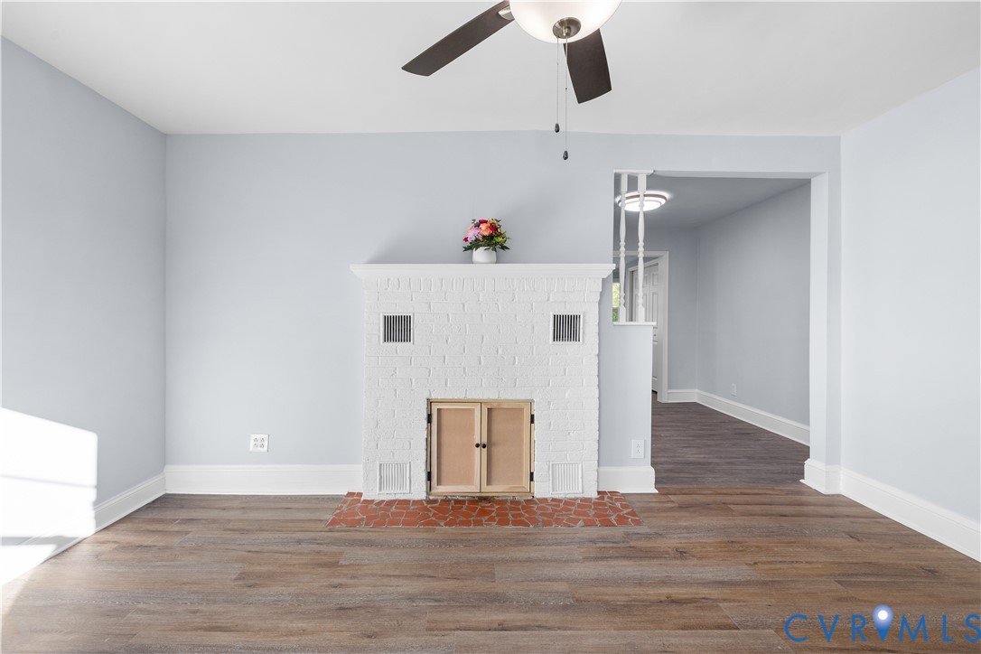 Wood-finish flooring, white brick fireplace with terracotta hearth, ceiling fan, and painted light blue walls