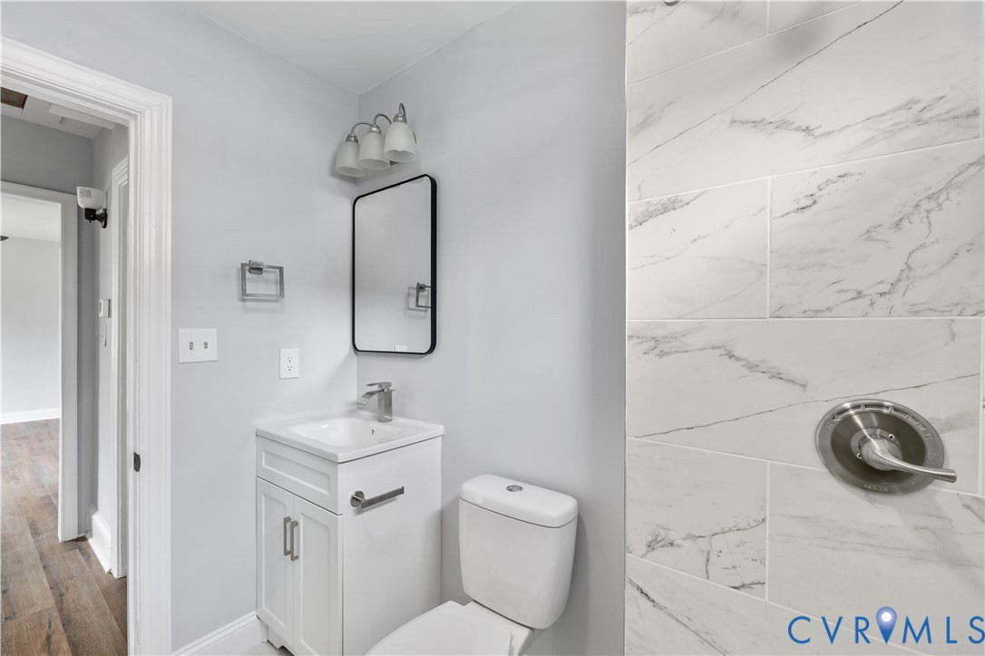 White vanity with integrated sink, rectangular mirror, three-light vanity fixture, and tiled shower surround with brushed nickel fixtures White vanity with integrated sink, rectangular mirror, three-light vanity fixture, and tiled shower surround with brushed nickel fixtures