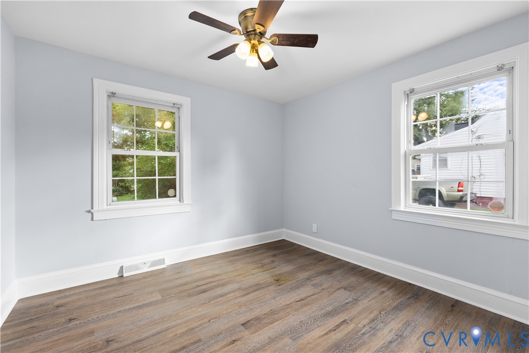 Wood-finish flooring, light blue walls, two multi-pane windows with white trim, and a ceiling fan with integrated lighting