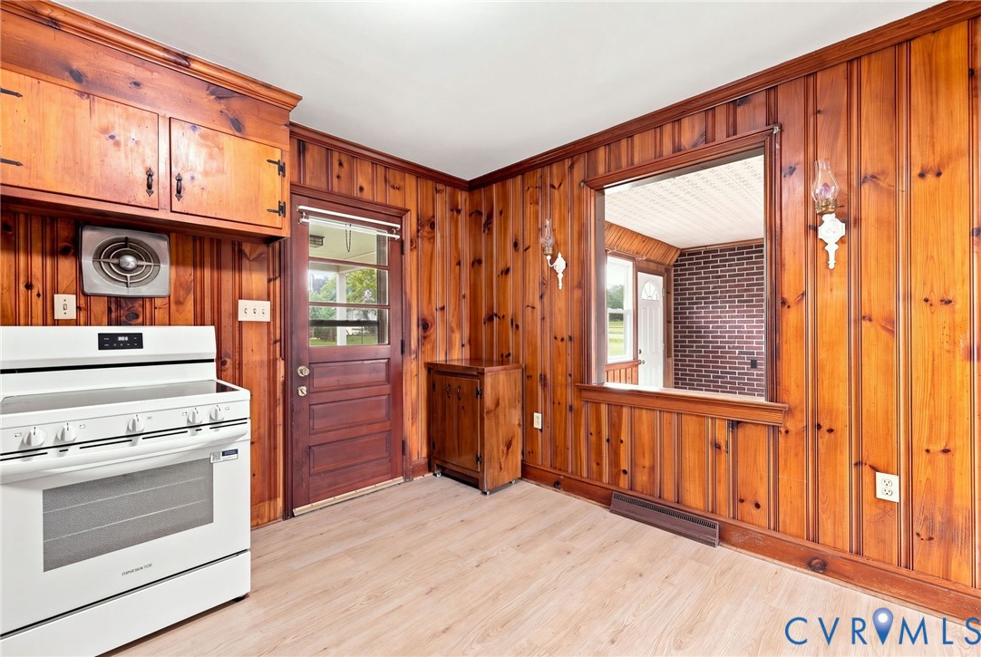 Wood paneling throughout, built-in wooden cabinetry, white freestanding range, light wood-finish flooring, and a pass-through window