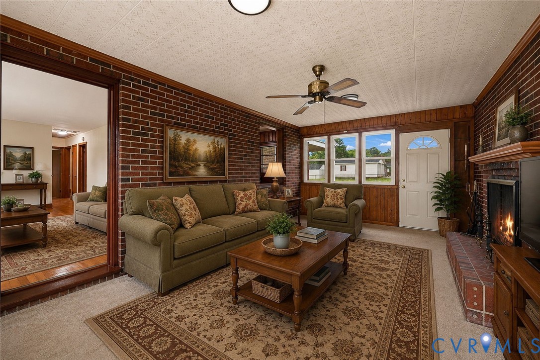 Brick accent wall, wood-paneled fireplace, multi-pane windows, ceiling fan, and a white entrance door
