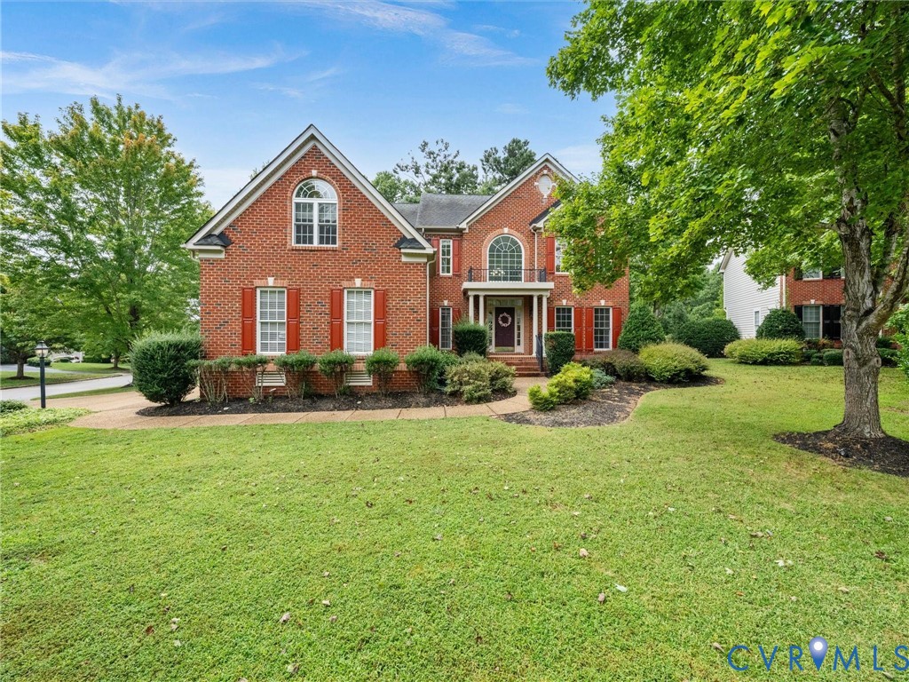 Brick exterior with red shutters, arched entry with balcony, gabled roof, and established landscaping