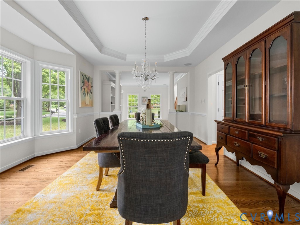 Hardwood flooring, bay window with multiple panes, elegant chandelier, tray ceiling, and white wainscoting