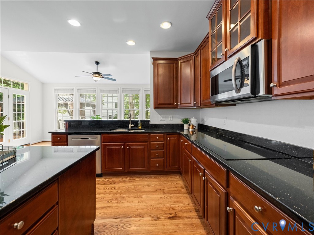 Kitchen featuring dark wood cabinetry, a built-in stainless steel microwave, black countertops, and wood-finish flooring