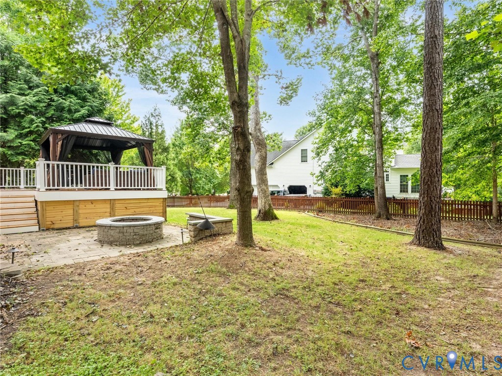 Expansive backyard featuring a built-in stone fire pit, wood deck with white railing, and a permanent gazebo structure