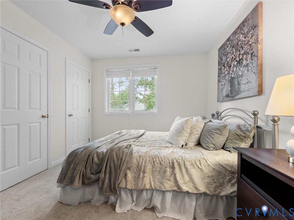 Serene primary bedroom featuring a metal bed frame, dual closets with six-panel doors, ceiling fan with integrated lighting, carpet flooring, and natural light from a multi-pane window