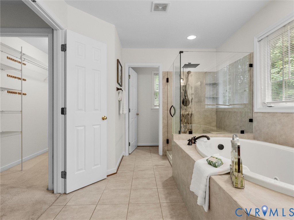 Spacious bathroom featuring a built-in tub, separate glass-enclosed shower, tiled flooring, and a walk-in closet with wire shelving