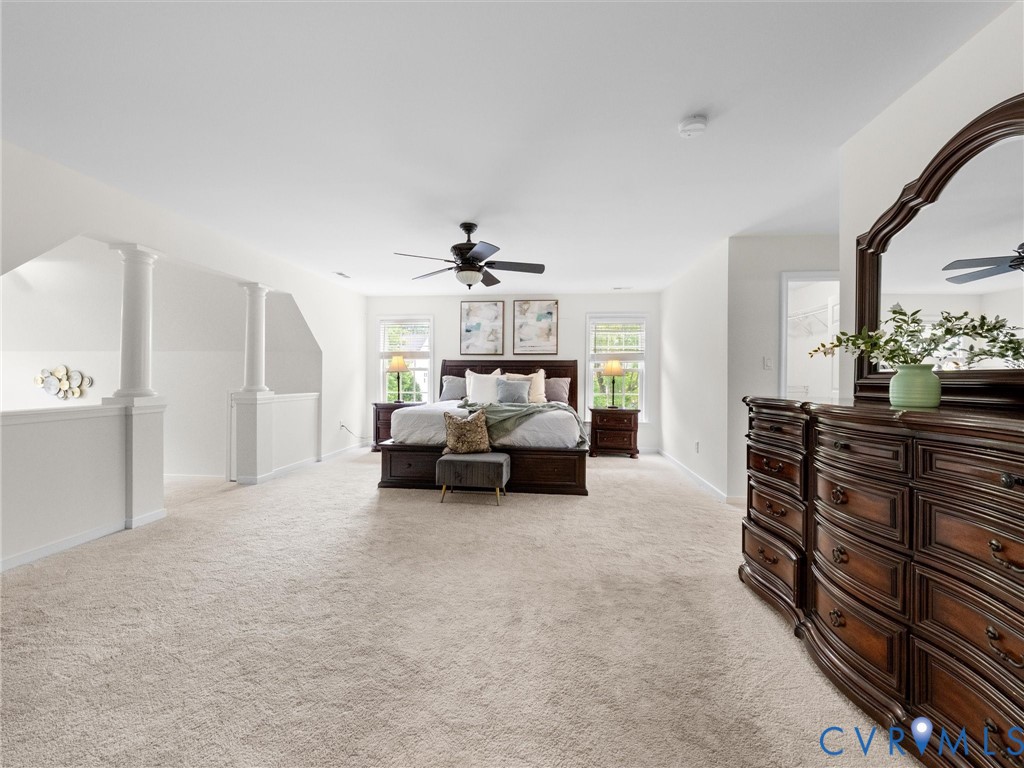 Spacious carpeted room featuring a ceiling fan, multiple windows, and a partial balustrade with decorative columns